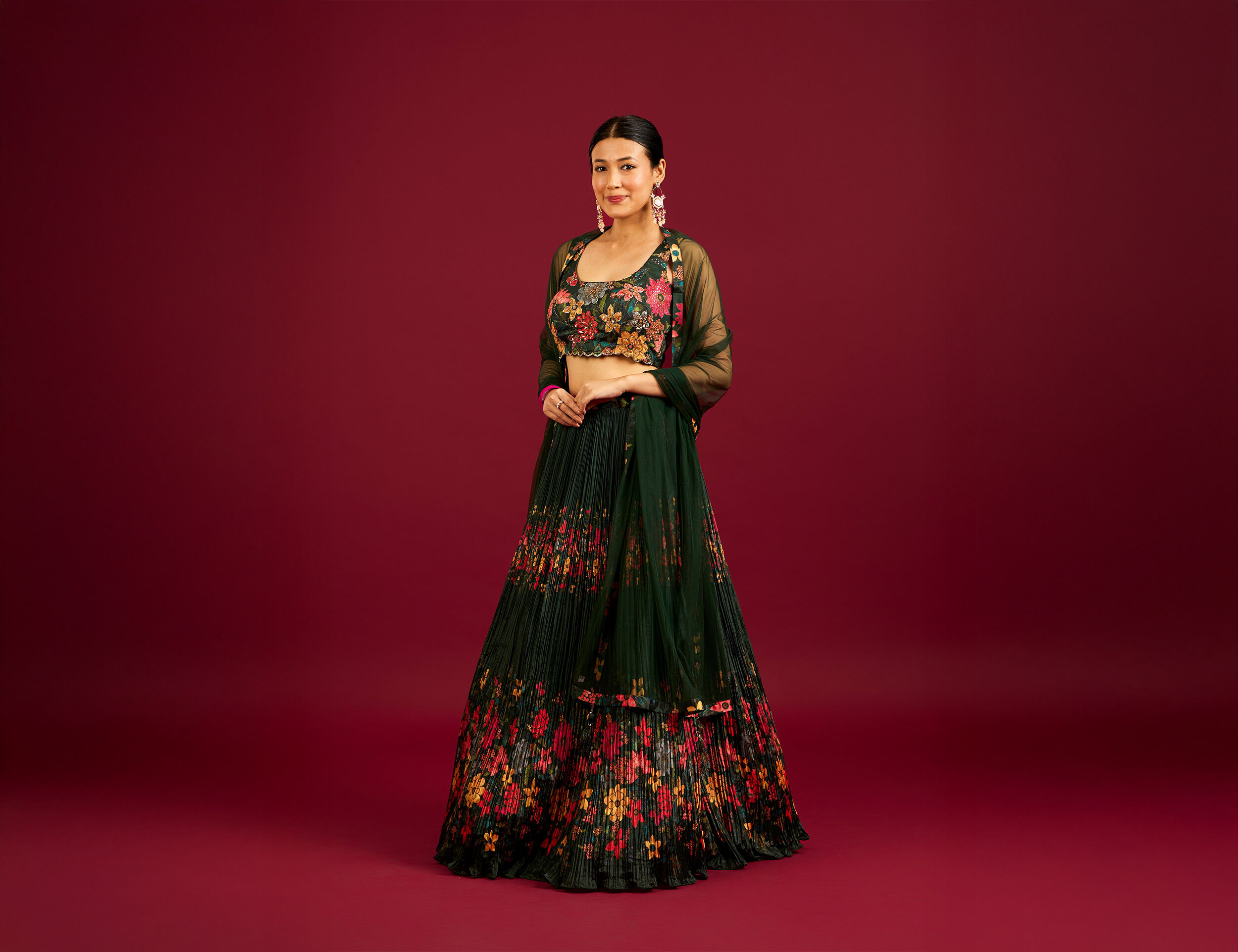 A woman elegantly dressed in a black floral lehenga featuring intricate and colorful floral patterns