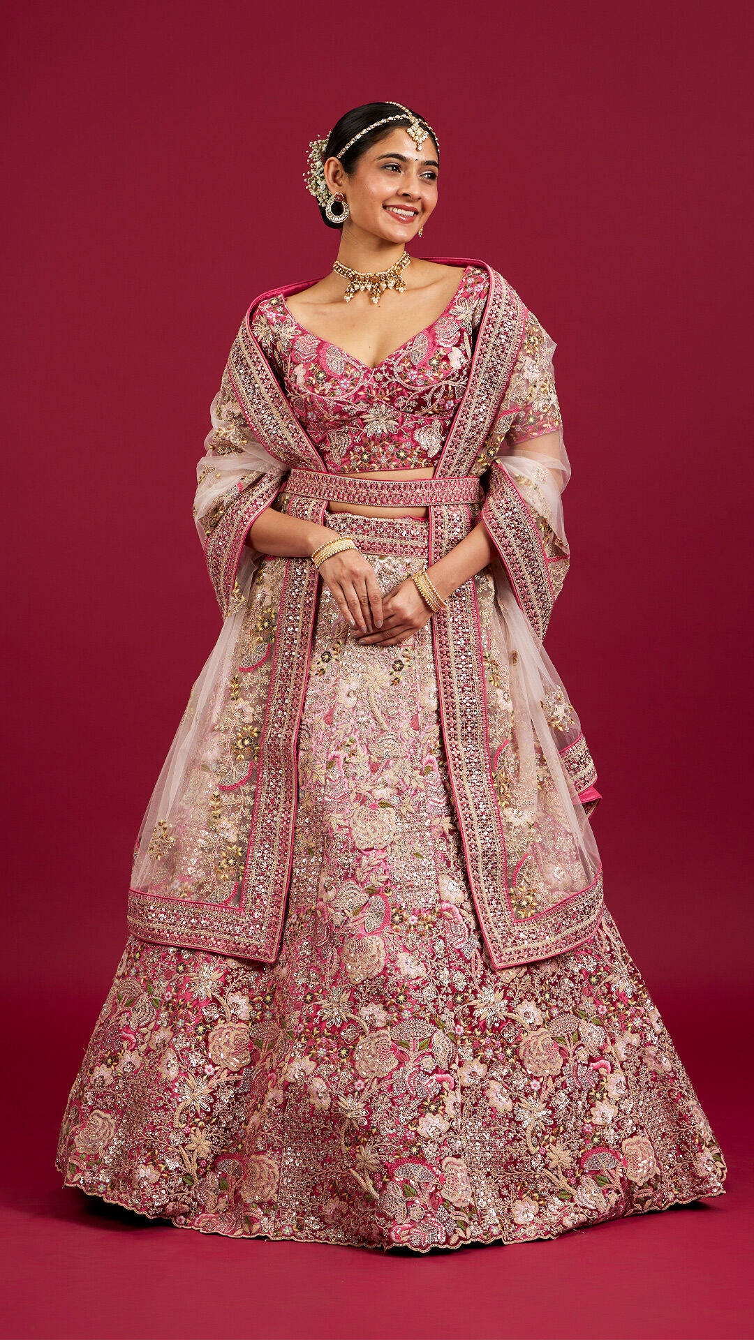 A woman showcasing a stunning pink floral lehenga beautifully embellished with colorful floral motifs.