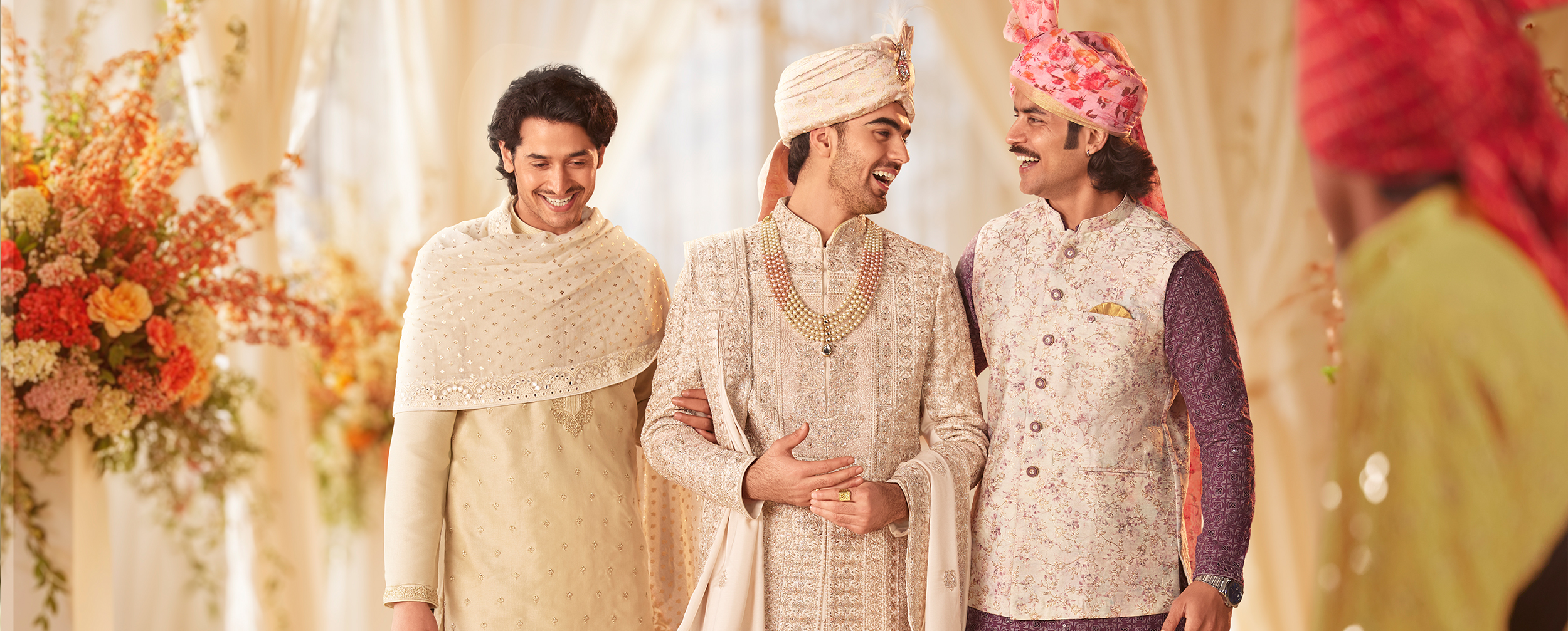 Three men in traditional Indian wedding attire, including ornate sherwani and kurta pajamas, smiling and talking in an elegant wedding setting Three men in traditional Indian wedding attire, including ornate sherwani and kurta pajamas, smiling and talking in an elegant wedding setting