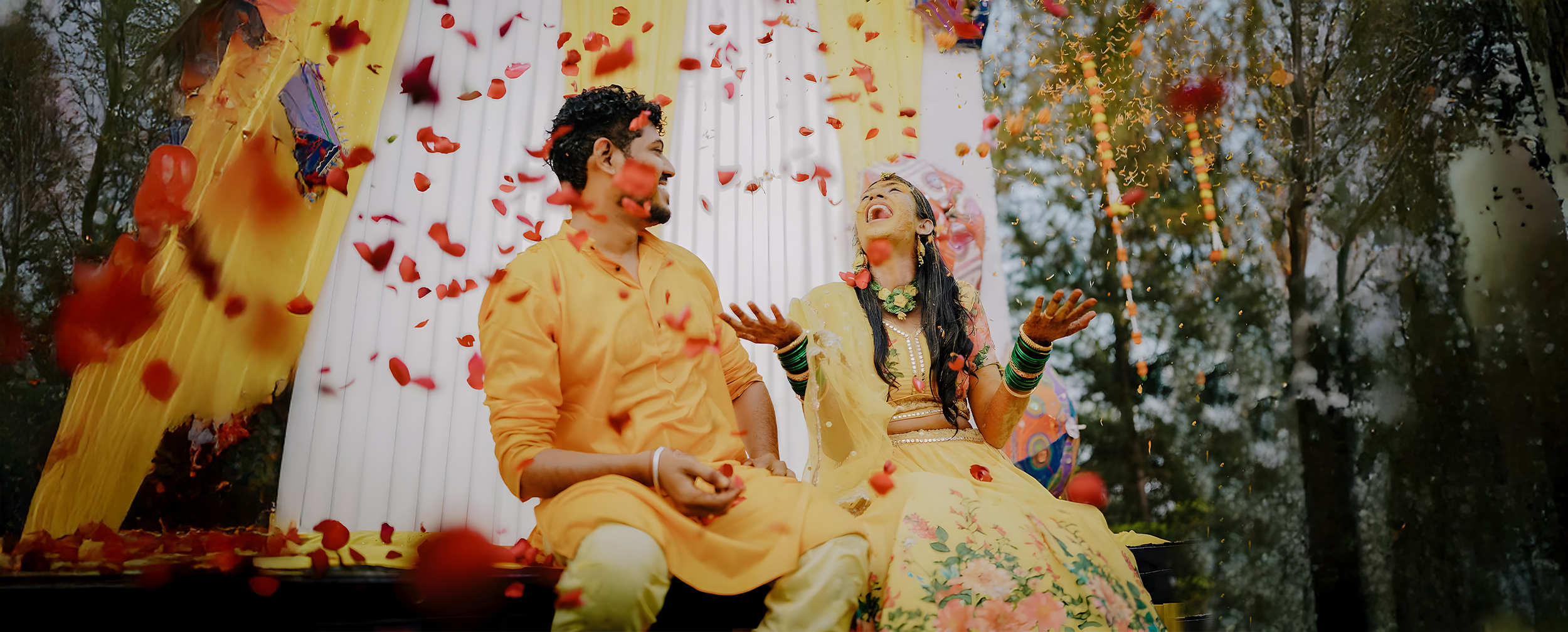 Bride and groom celebrating haldi with flowers, laughter, and festive d&eacute;cor