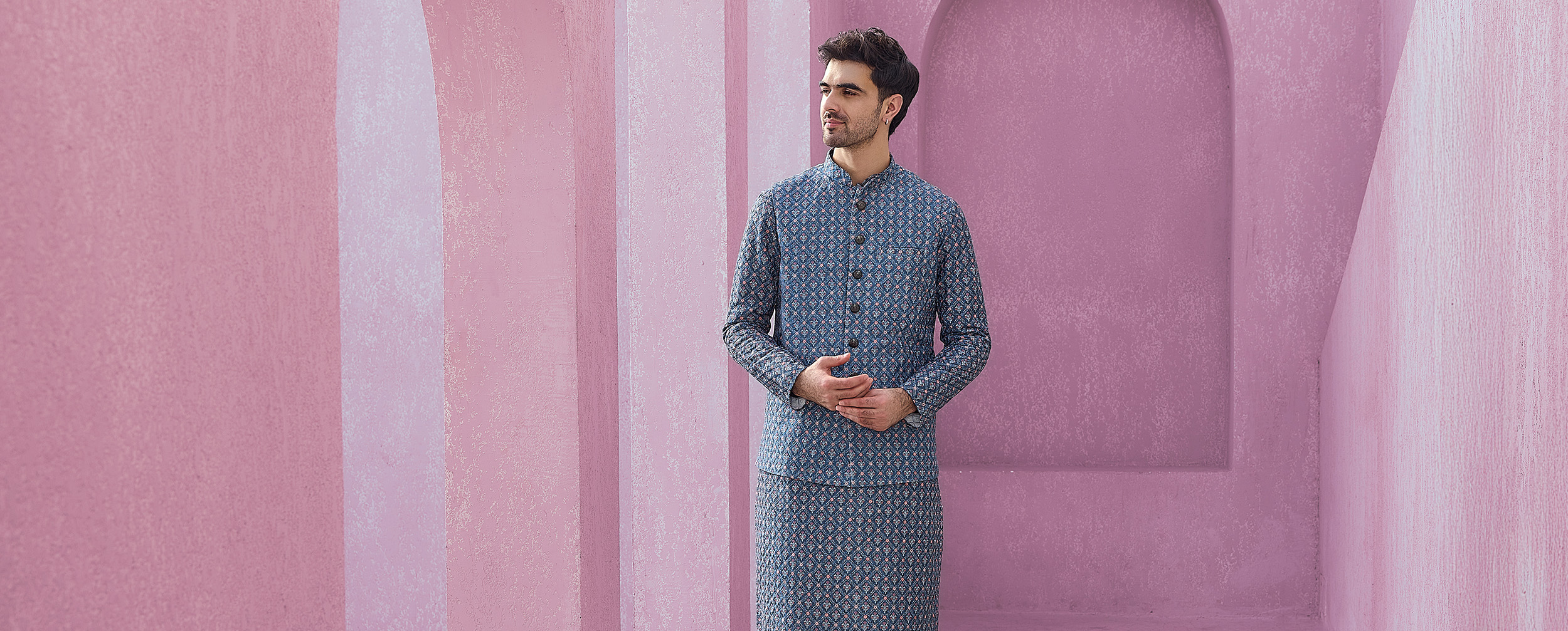 Man in a patterned blue and black kurta set with a Nehru jacket and black slip-on shoes.