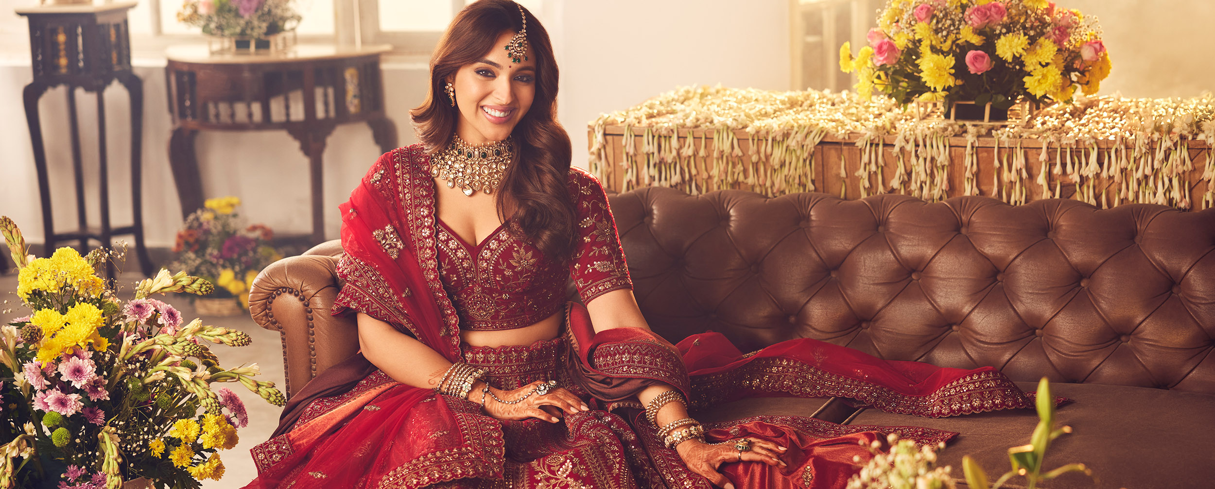 Indian bride in a heavily embroidered red velvet lehenga, sitting on a leather sofa with traditional jewelry. Indian bride in a heavily embroidered red velvet lehenga, sitting on a leather sofa with traditional jewelry.