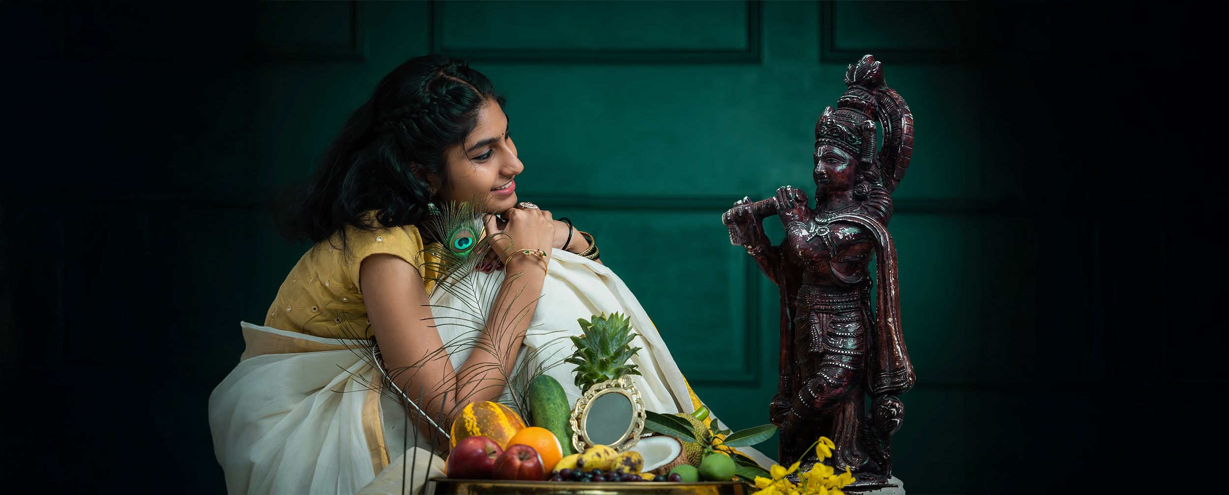 Young girl dressed in traditional attire admiring a Lord Krishna idol, with fruits and festive decor arranged for Krishna Janmashtami celebration
