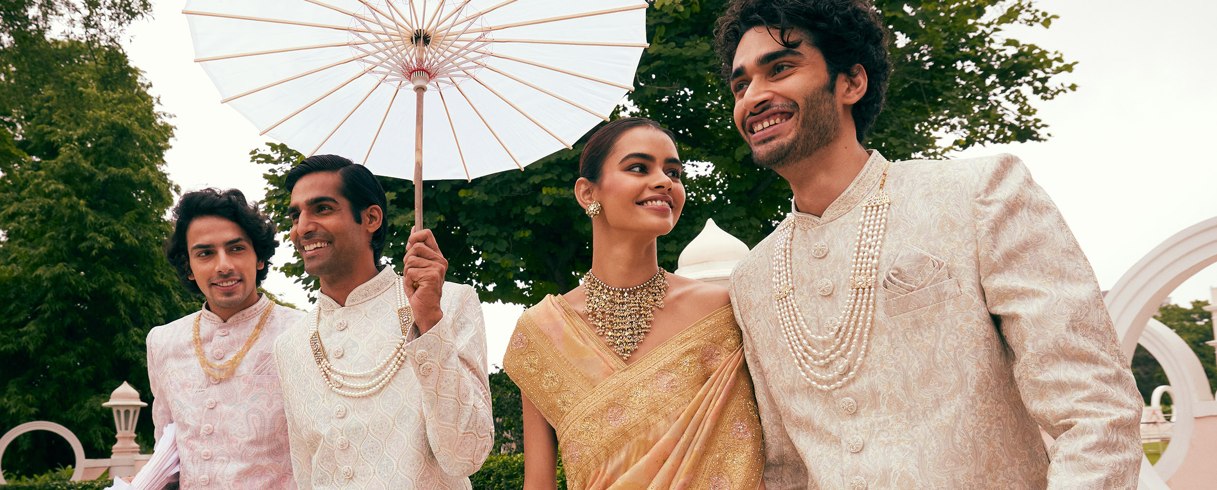 Groom, bride, and friends wearing moti malas and posing with a traditional umbrella at a royal-themed wedding Groom, bride, and friends wearing moti malas and posing with a traditional umbrella at a royal-themed wedding