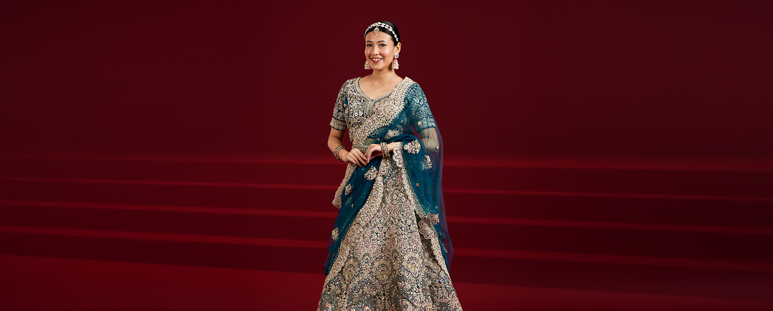  Woman in an emerald green flowing anarkali with mirror work, standing next to a man in an embroidered jacket, highlighting festive wear.
