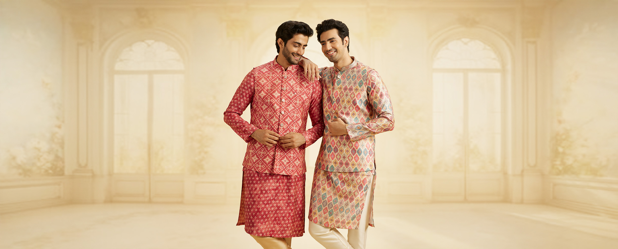 Two men smiling in red patterned kurta jacket sets and multicolored geometric print kurtas, ideal for a Sangeet. Two men smiling in red patterned kurta jacket sets and multicolored geometric print kurtas, ideal for a Sangeet.