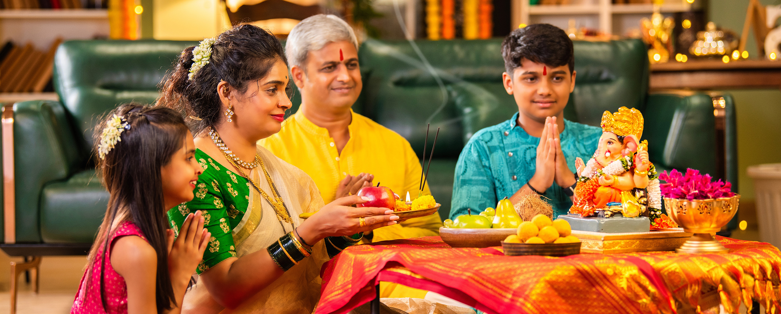 Indian family performing Ganesh Chaturthi puja at home with offerings of fruits and sweets, praying to Lord Ganesha idol on a decorated table Indian family performing Ganesh Chaturthi puja at home with offerings of fruits and sweets, praying to Lord Ganesha idol on a decorated table