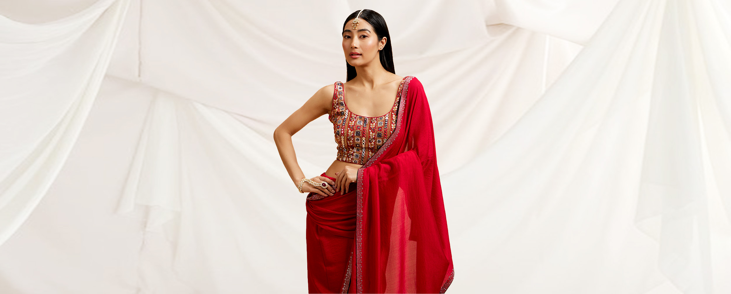 Woman in a vibrant red chiffon saree with an elaborately embroidered multicolor blouse and maang tikka.  Woman in a vibrant red chiffon saree with an elaborately embroidered multicolor blouse and maang tikka.