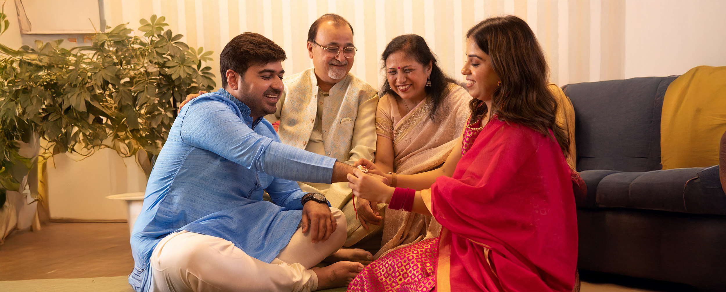 Family celebrating Raksha Bandhan at home, with siblings in colorful traditional festive outfits during the rakhi ceremony.
