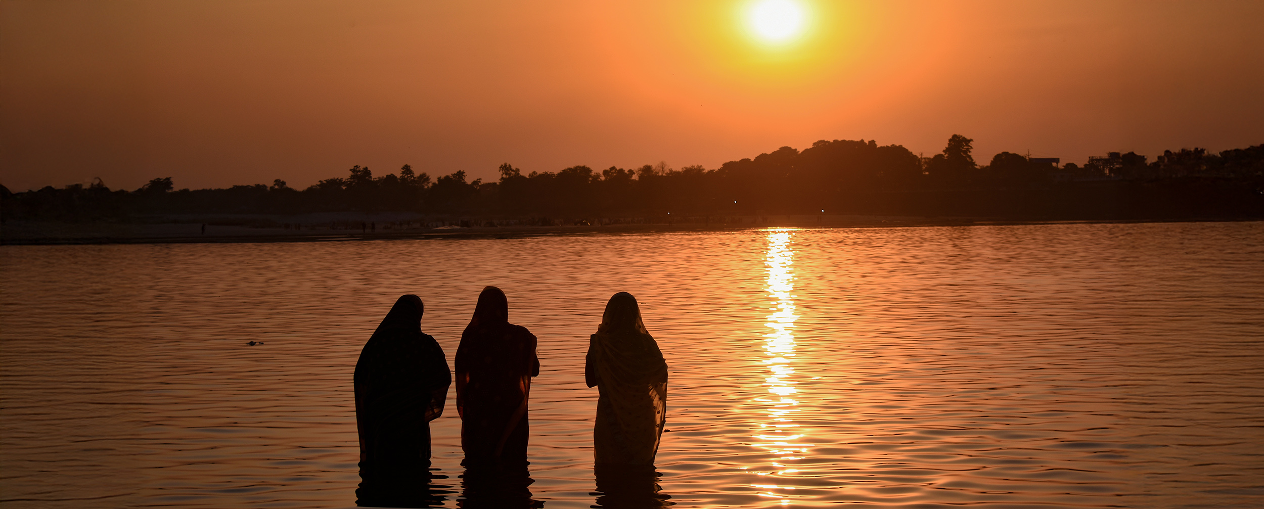 A devotee making the traditional *arghya* offering to the setting or rising sun, a central Chhath Puja ritual.