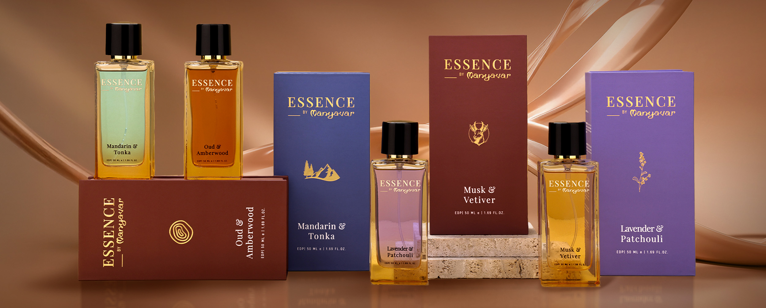 Essence by Manyavar perfume collection featuring Mandarin & Tonka, Oud & Amberwood, Musk & Vetiver, and Lavender & Patchouli fragrances displayed on a brown background