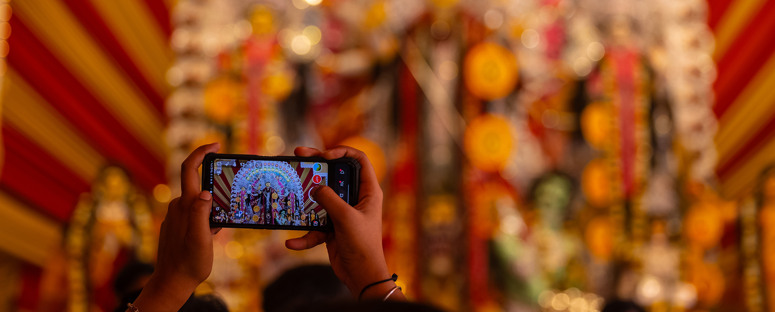 Devotee capturing Durga idol on smartphone during Navratri celebration with colorful decorations in the background