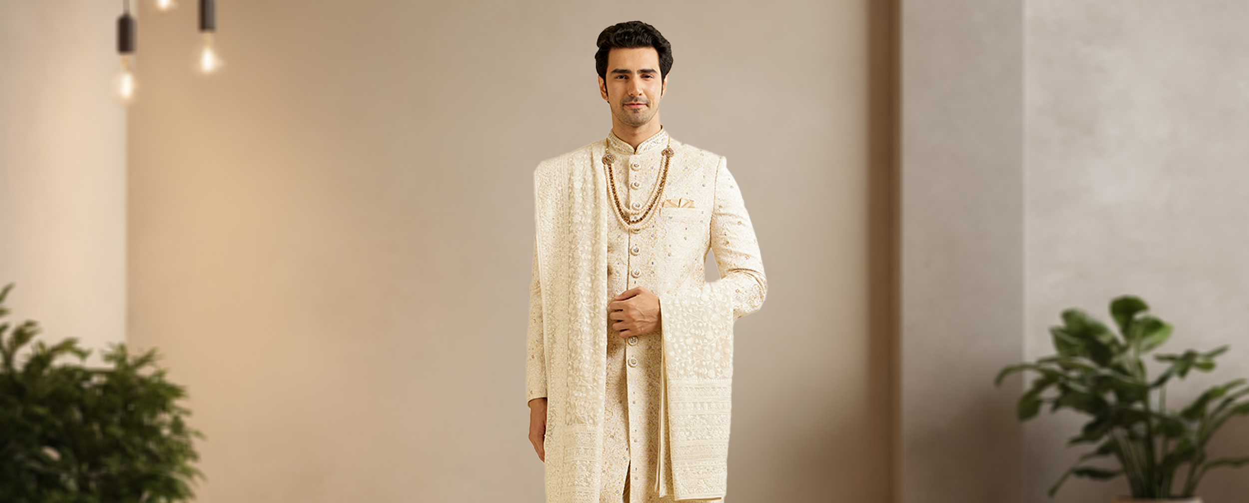 Groom in an embroidered cream sherwani with an elaborate matching shawl and beaded necklace.