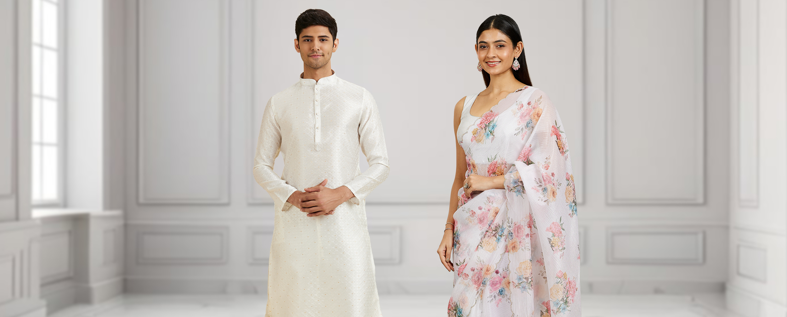 Man in cream‑white silk kurta and woman in pastel floral saree standing side by side in a bright, elegant hall-modern Onam outfits for men and women 2025. Man in cream‑white silk kurta and woman in pastel floral saree standing side by side in a bright, elegant hall-modern Onam outfits for men and women 2025.