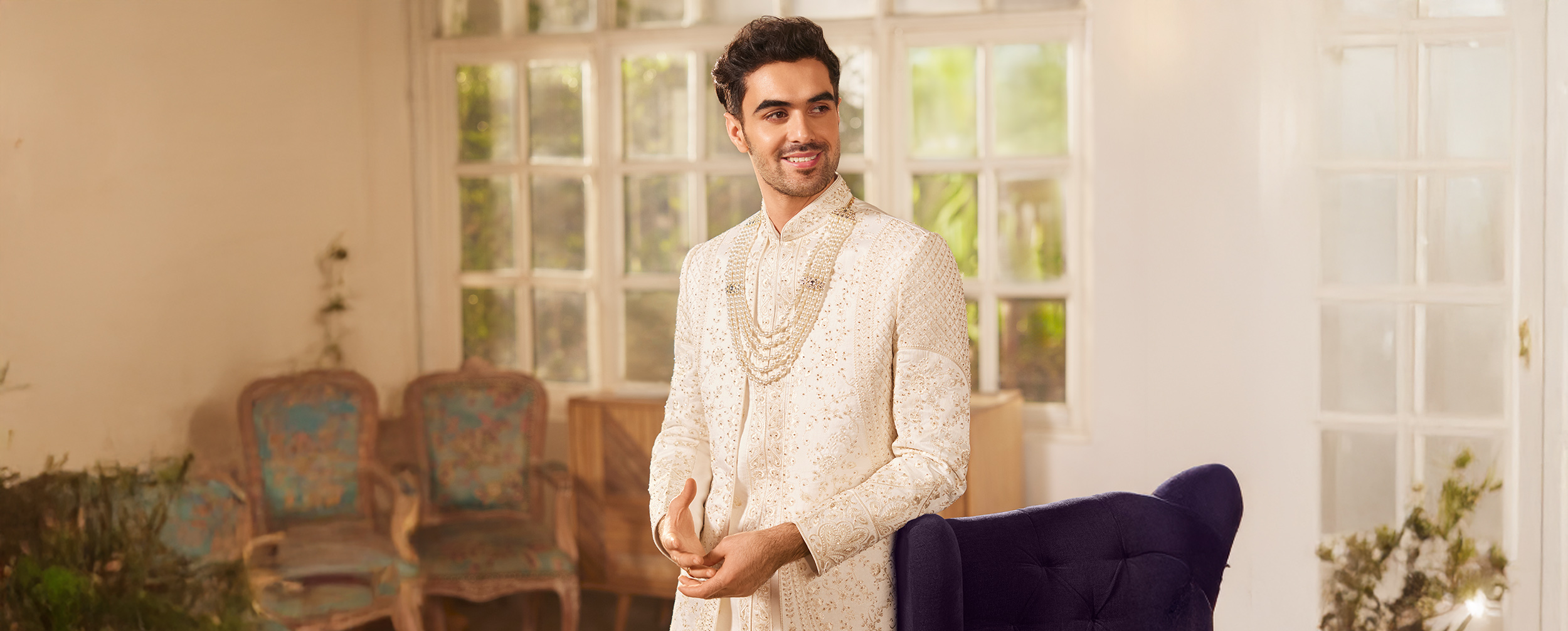 Stylish groom in cream sherwani posing indoors, highlighting trending wedding fashion for men Stylish groom in cream sherwani posing indoors, highlighting trending wedding fashion for men