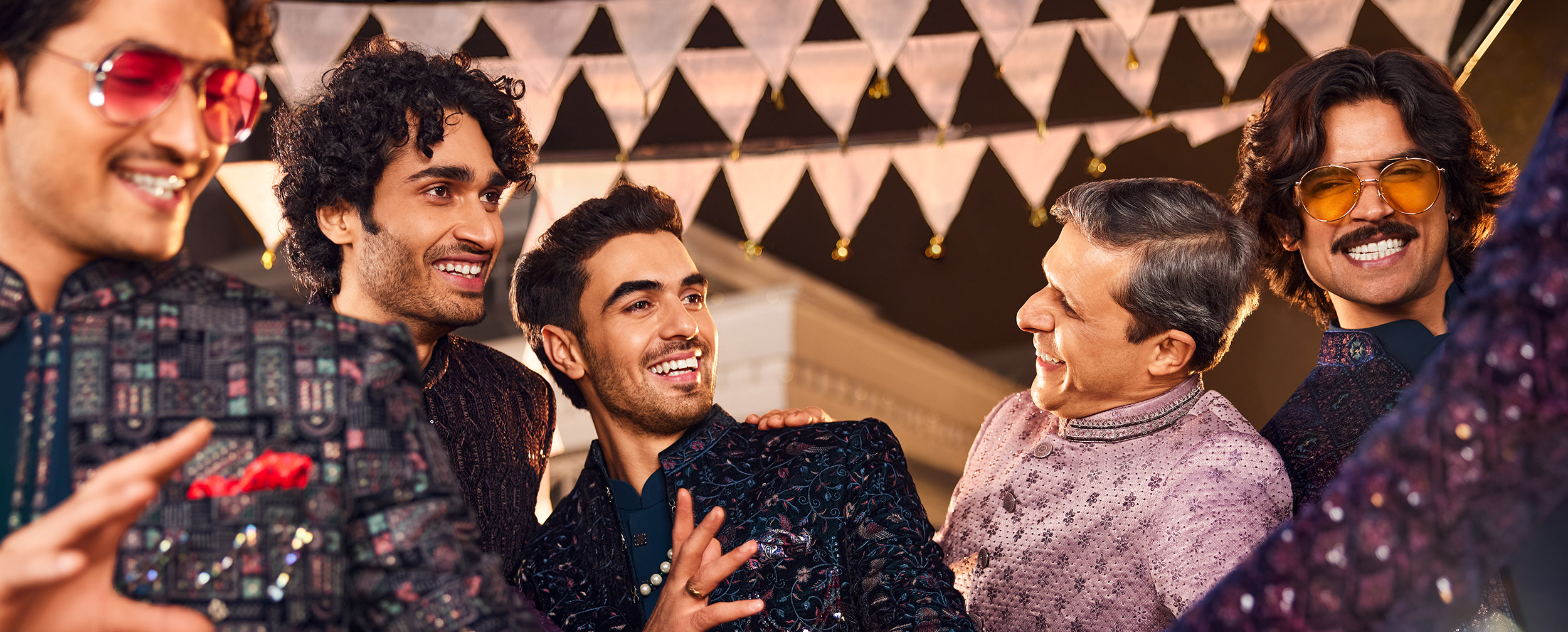 Group of men dancing and smiling in heavily embroidered Bandhgala jackets for a Sangeet celebration.