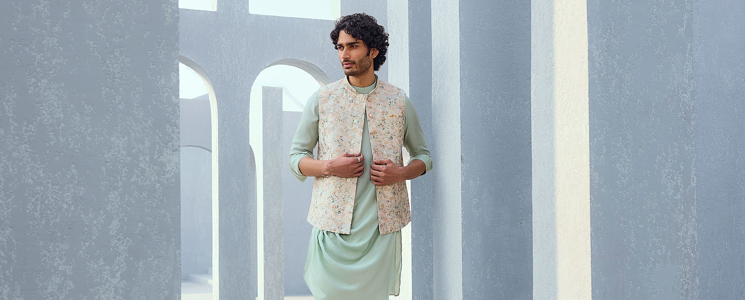 Man in a mint green draped kurta and cream floral print Nehru jacket. Man in a mint green draped kurta and cream floral print Nehru jacket.