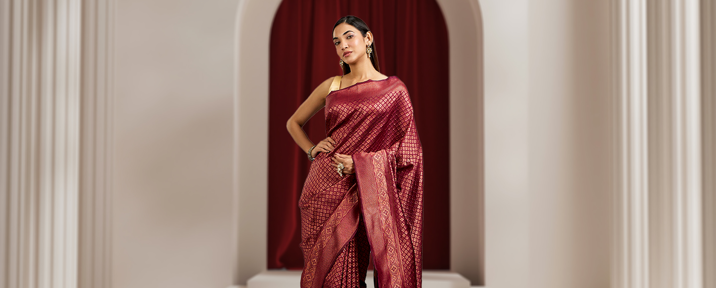 Woman draped in a maroon silk Banarasi saree with gold brocade work, showcasing a regal reception style.