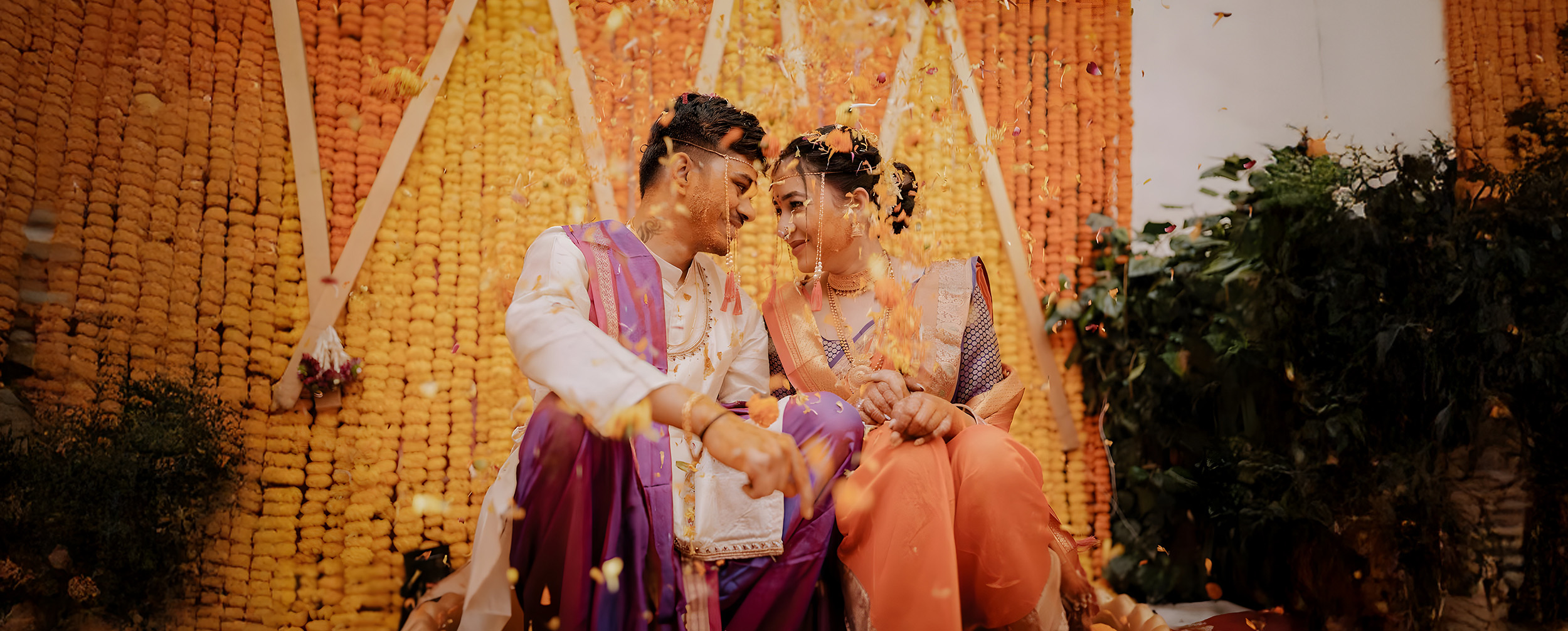 Indian wedding couple in traditional Marathi attire (Navari saree and dhoti), with flower petals falling on them against a marigold backdrop.  Indian wedding couple in traditional Marathi attire (Navari saree and dhoti), with flower petals falling on them against a marigold backdrop.