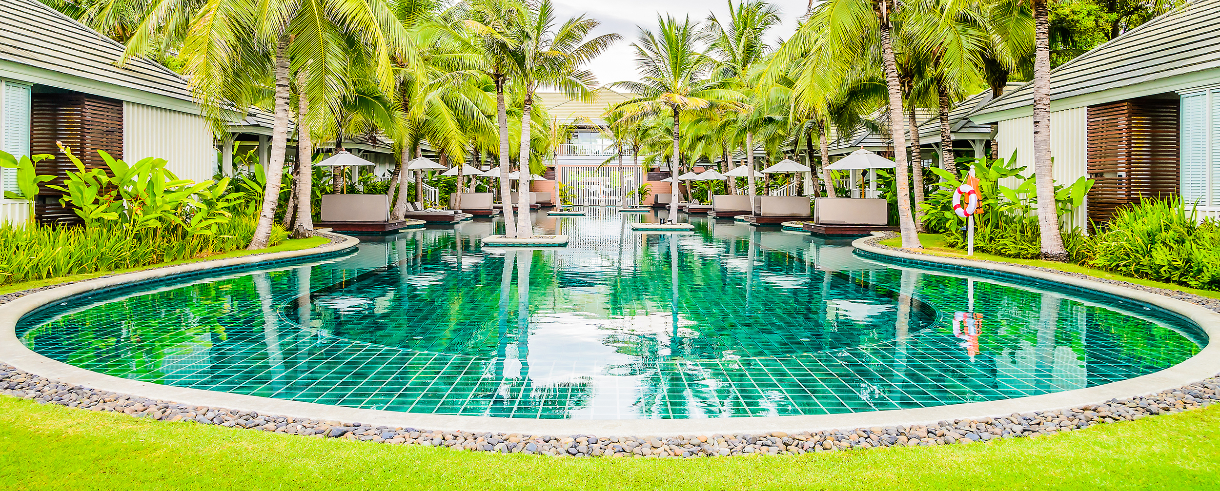 Luxurious wedding pool party venue with crystal-clear turquoise pool, surrounded by palm trees, green lawns, and private cabanas — tropical celebration setting. Luxurious wedding pool party venue with crystal-clear turquoise pool, surrounded by palm trees, green lawns, and private cabanas — tropical celebration setting.