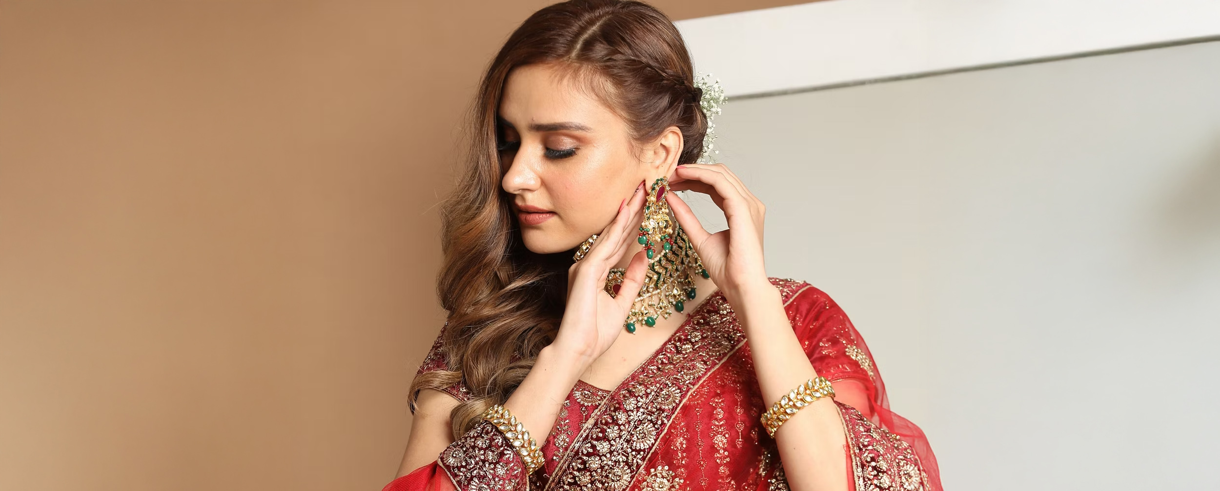Woman in a red embellished saree wearing festive jewellery and adjusting heavy earrings for Durga Puja